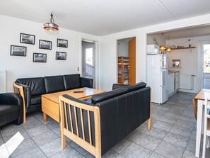 Un salon moderne avec un canapé, une table en bois et un coin cuisine équipé d’un réfrigérateur.