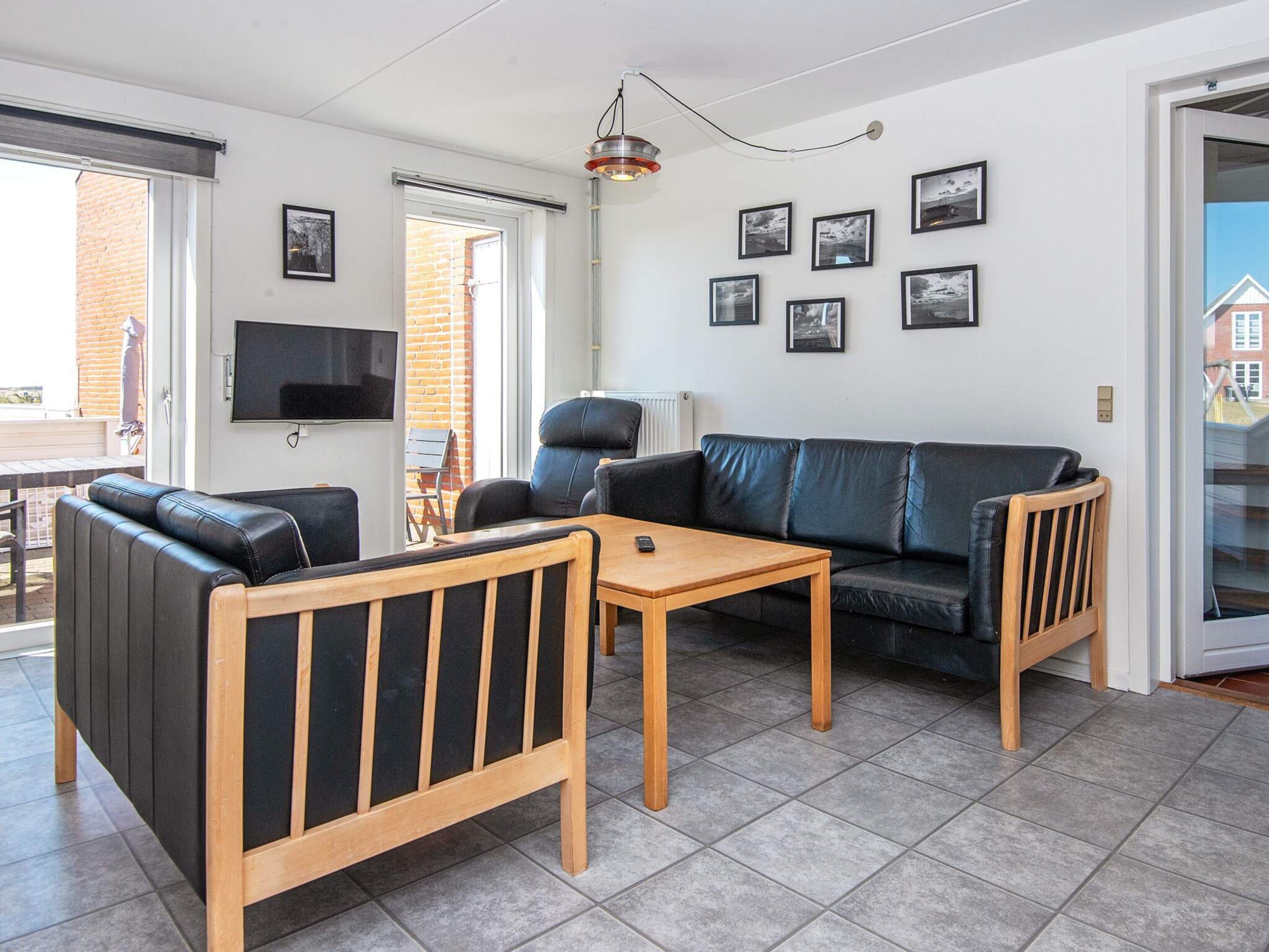 Ein modernes Wohnzimmer mit einer Couch, einem Sessel und einem Couchtisch. Ein Fernseher ist an der Wand montiert und ein Fenster bietet Blick auf ein Backsteingebäude.