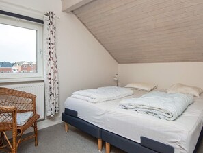 A bedroom with a bed, a chair, a window with curtains, and a view of buildings outside.