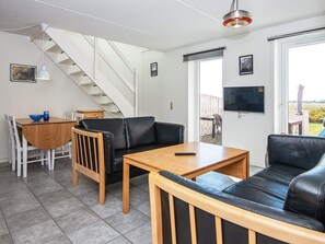 Un salon moderne avec un escalier, un coin repas et un téléviseur fixé au mur.