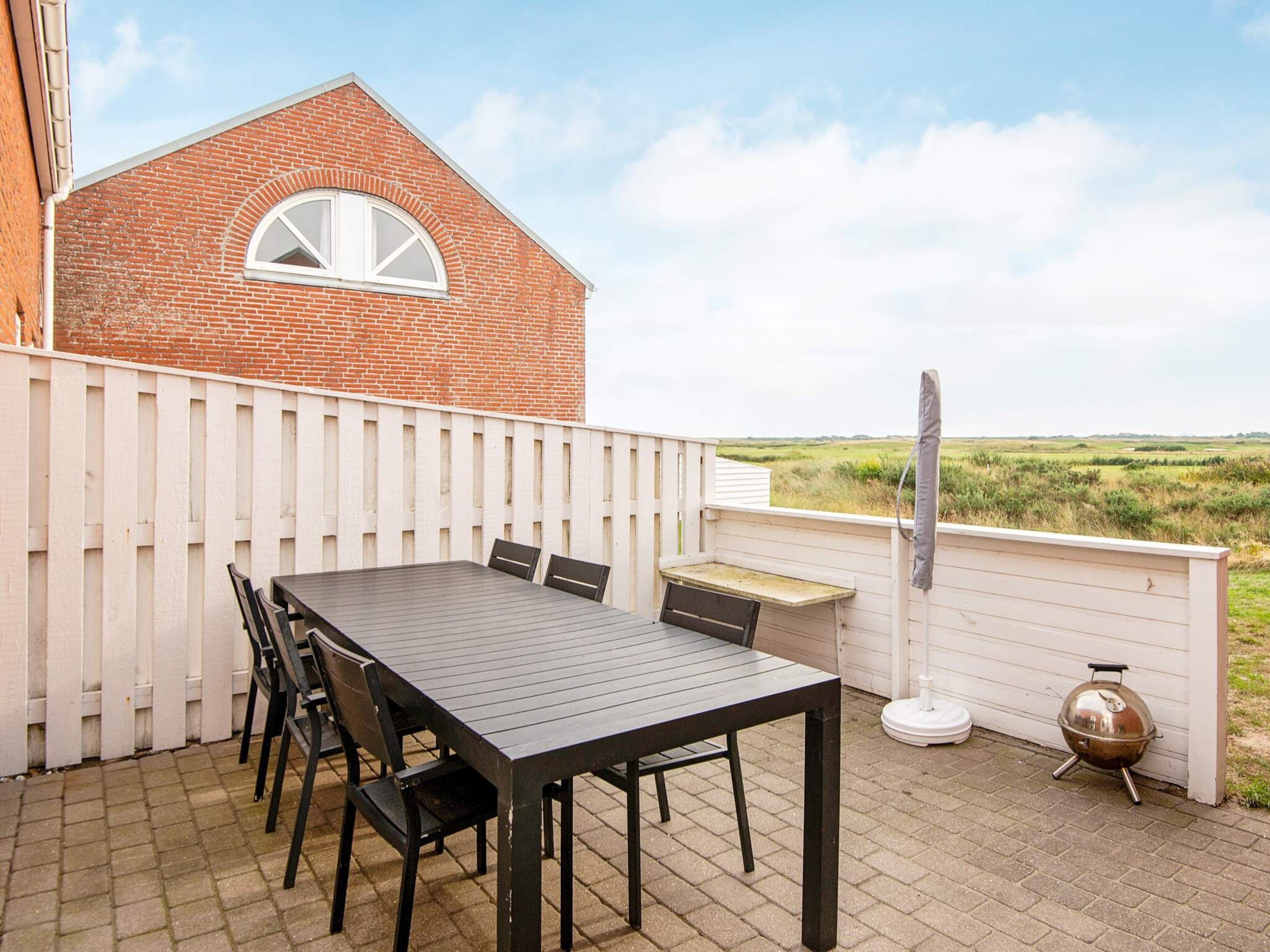 A patio with a table and chairs, a barbecue grill, and a view of a field.
