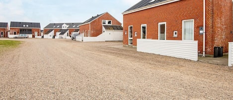 A gravel driveway leading to a row of red brick buildings with white railings and a clear sky.