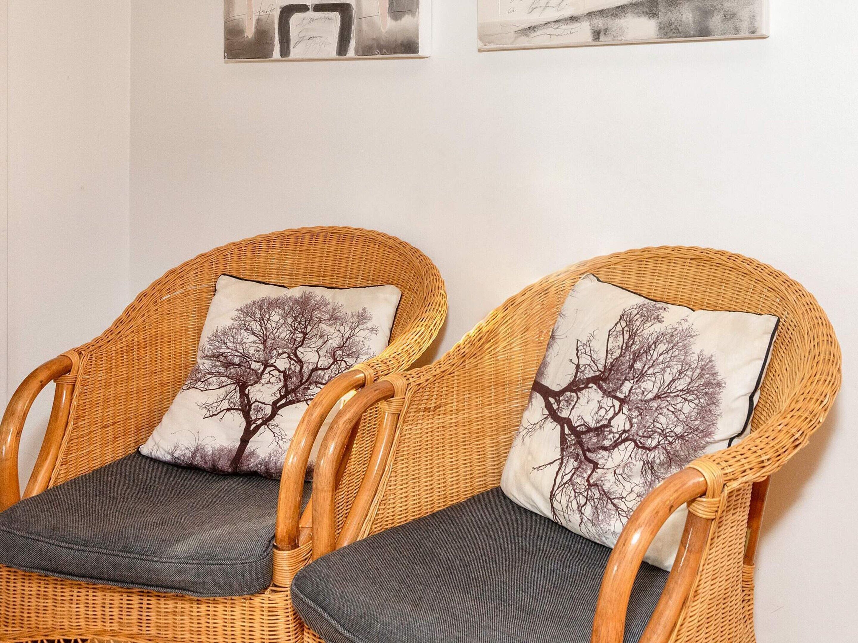 Två fåtöljer i rotting med gråa kuddar och en vägg med inramade konstverk.