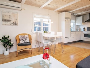 Una cocina moderna con armarios blancos, horno empotrado y una zona de comedor con mesa y sillas blancas.