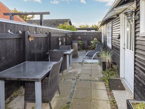 A patio area with outdoor furniture, a wooden fence, and a house with a white door. - 4 Star Holiday Home in Skagen (Skagen)