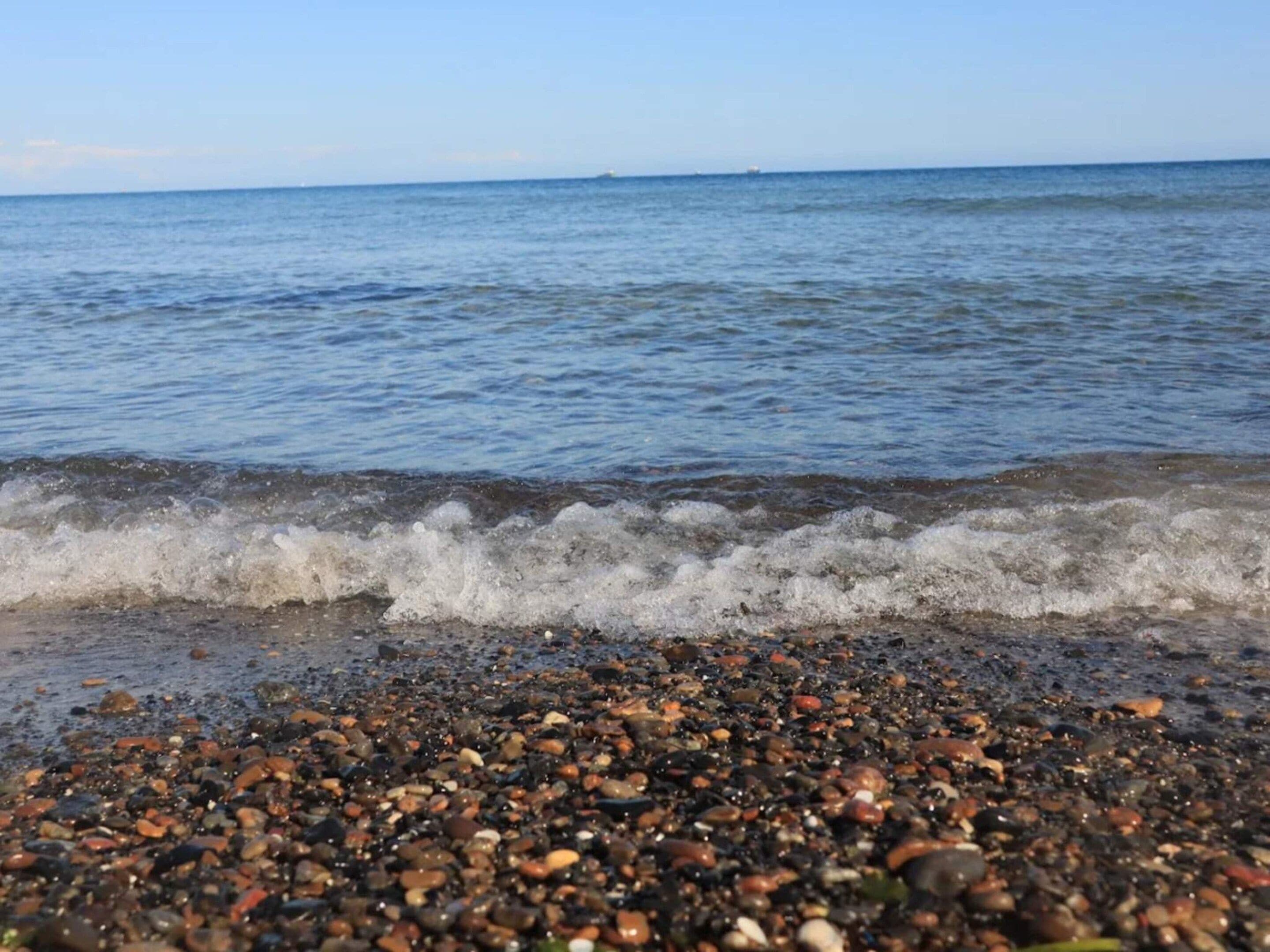 Een kiezelstrand met golven, heldere lucht en een rustige zee.