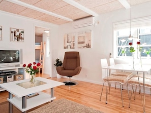 A modern living room with a flat-screen TV, a brown armchair, a glass coffee table, and a dining area with white chairs. - 4 Star Holiday Home in Skagen (Skagen)