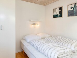 A single bed with a floral-patterned duvet, a bedside table, and a wall-mounted light fixture. - 4 Star Holiday Home in Skagen (Skagen)
