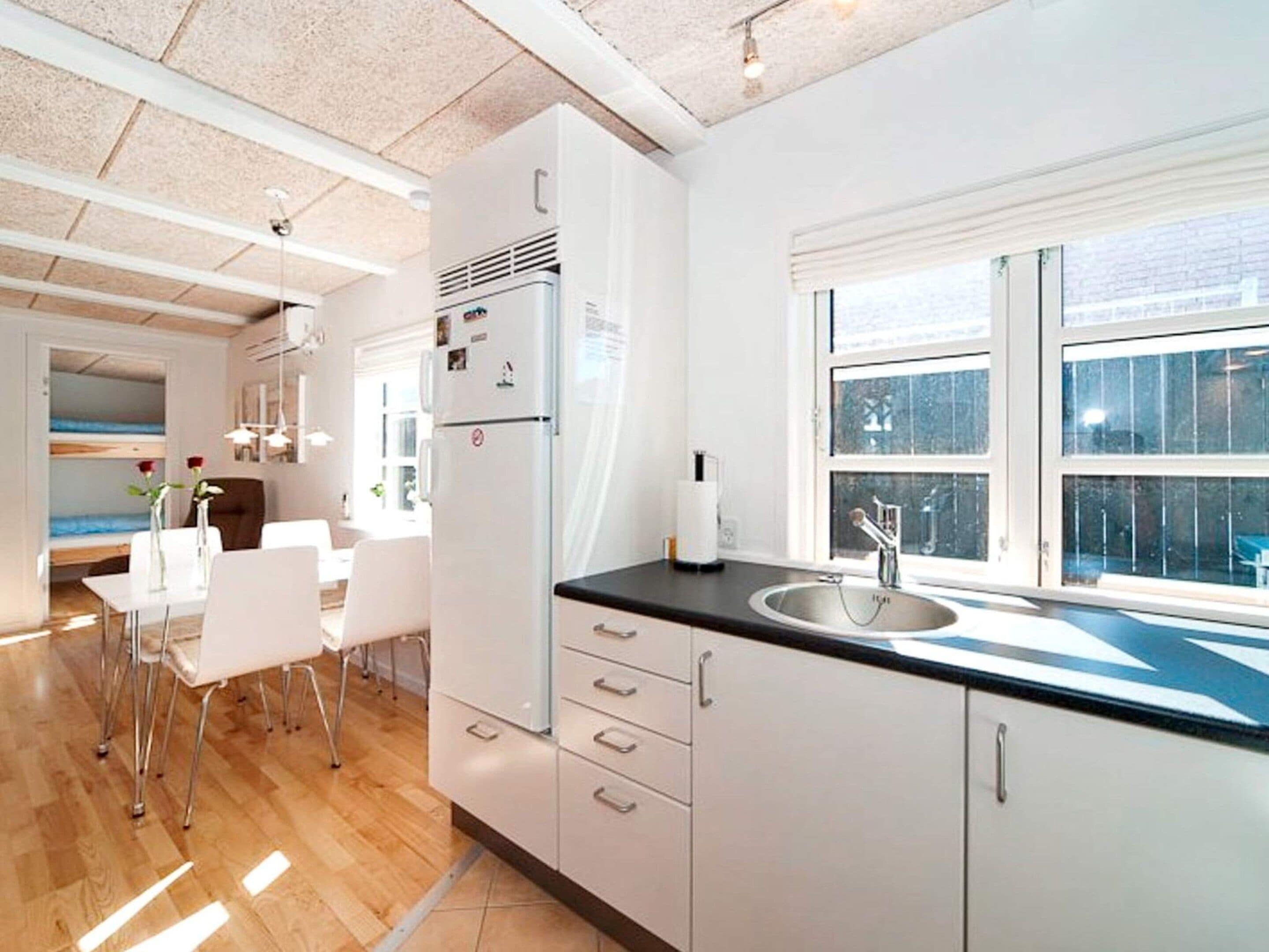 Une cuisine moderne dotée d’une grande fenêtre, de meubles blancs et d’un coin repas avec une table et des chaises.