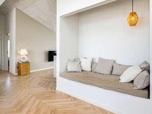 A modern living room with a wooden floor, a white sofa with cushions, a lamp on a wooden side table, and a television on the wall.