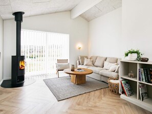 A living room with a wood-burning stove, a sofa, a coffee table, and a bookshelf. - 5 Star Holiday Home in Hjorring (Hjørring)