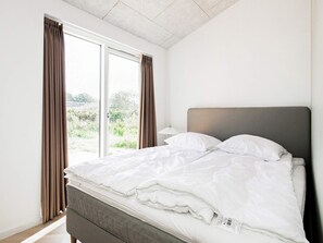 A bedroom with a bed, curtains, and a view of greenery outside.