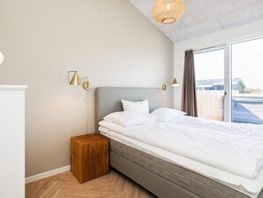 Un dormitorio moderno con una cama grande, lámparas de noche, una mesita de madera y vistas a través de un ventanal.