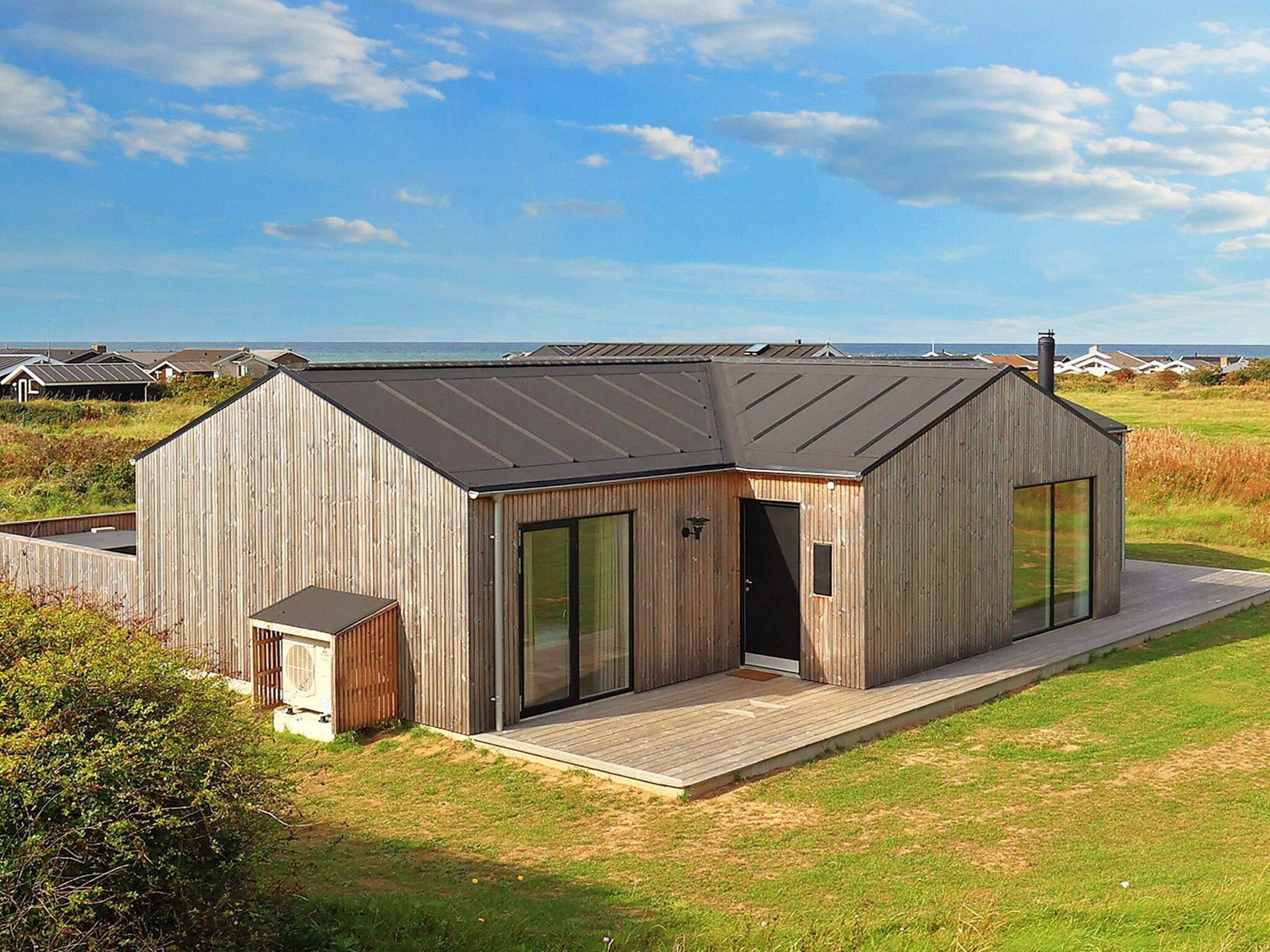 Una cabaña moderna de madera con techo inclinado, puertas de cristal amplias y una terraza.
