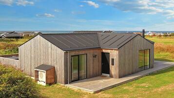 Una cabaña moderna de madera con techo inclinado, puertas de cristal amplias y una terraza.