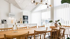 Una cocina moderna con armarios blancos, una gran mesa de comedor de madera y una lámpara colgante.