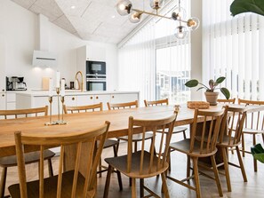 A modern kitchen with white cabinetry, a large wooden dining table, and a hanging light fixture. - 5 Star Holiday Home in Hjorring (Hjørring)