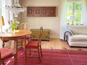 A room with a dining table, chairs, a sofa, a patterned rug, a chandelier, and a window with curtains. - 9 Person Holiday Home in Ronneby (Listerby)