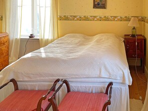 Ein Schlafzimmer mit einem Bett, einem Nachttisch, einer Lampe, einem Sessel und einem Fenster mit Vorhängen.