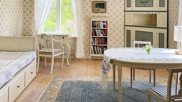 Una habitación con cama, escritorio, silla, estantería y una mesa con un florero.