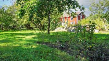 A red building with a stone wall and a grassy area with trees.