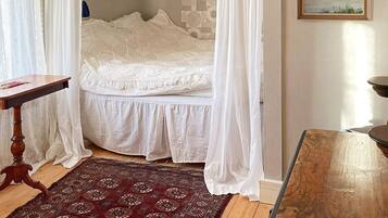 A bedroom with a bed, a wooden table, a patterned rug, and a painting on the wall.