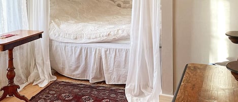 Un dormitorio con cama, una mesa de madera, una alfombra estampada y un cuadro en la pared.