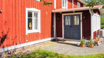 Una casa de madera roja con puerta azul oscuro, ventanas blancas y un pequeño porche con plantas en macetas.