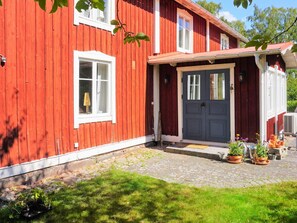 A red wooden house with a dark blue door, white windows, and a small porch area with potted plants. - 9 Person Holiday Home in Ronneby (Listerby)