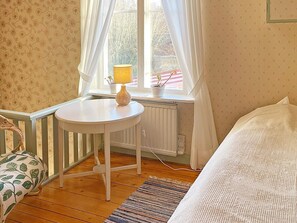 A small room with a white table, a window with curtains, a radiator, and a bed with a white bedspread. - 9 Person Holiday Home in Ronneby (Listerby)