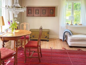 A room with a wooden dining table, chairs, a red patterned rug, a sofa, a small cabinet, and a window with a view of greenery. - Idyllic Family Retreat Close to the Sea (Listerby)