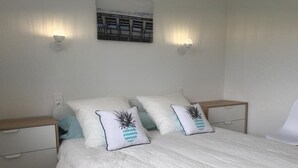 Una cama bien hecha con ropa blanca y dos almohadones decorativos, una lámpara de pared y un cuadro enmarcado sobre la cama.