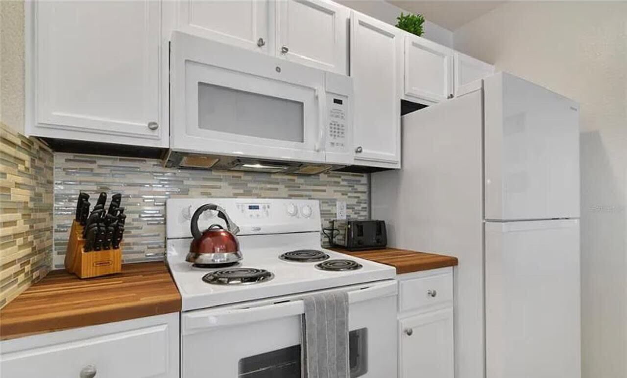 A compact kitchen with white cabinets, a stove, a microwave, a toaster, and a refrigerator.