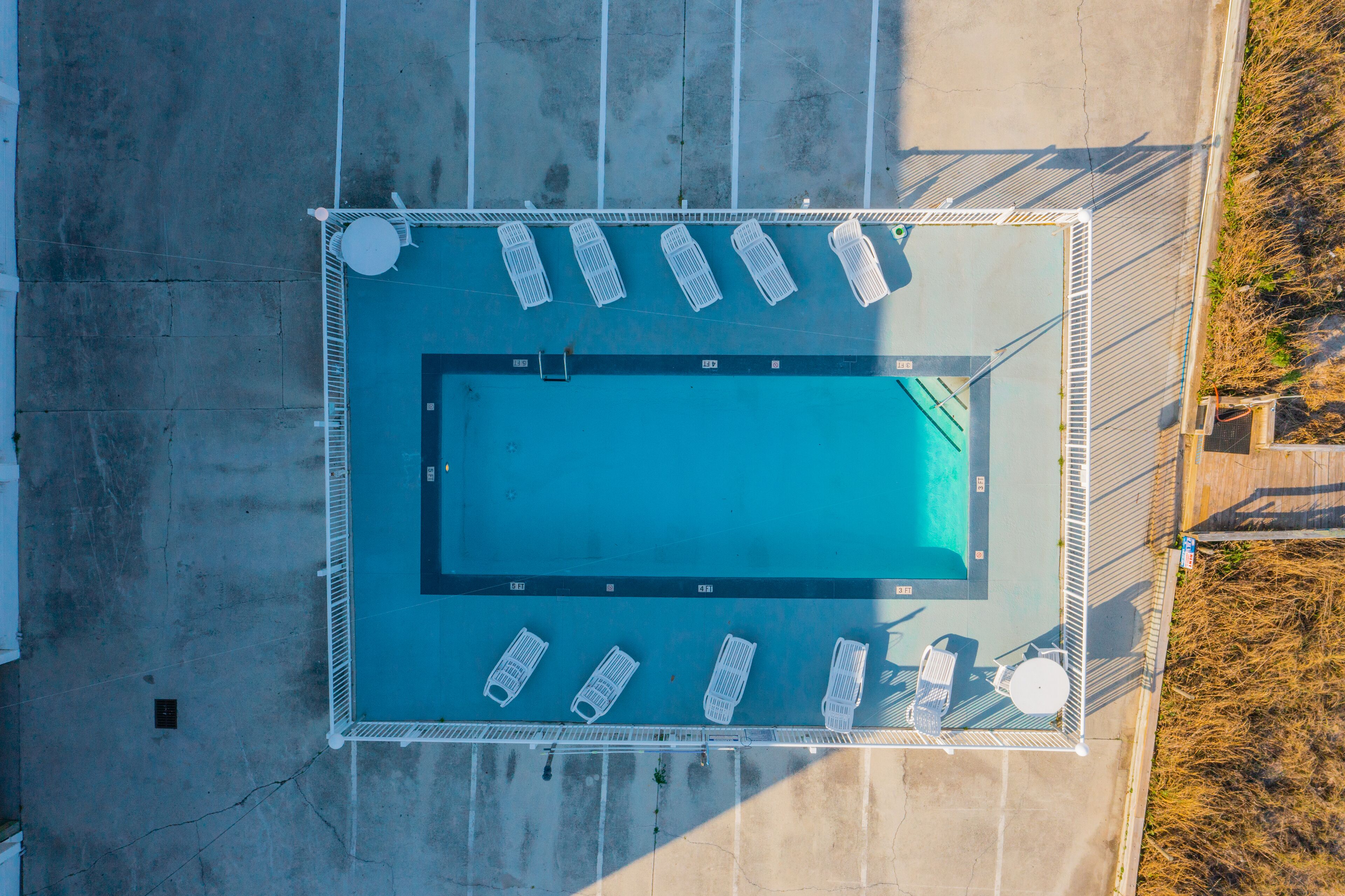 Vue aérienne d’une piscine rectangulaire entourée d’une terrasse aménagée avec des chaises longues et une petite table.