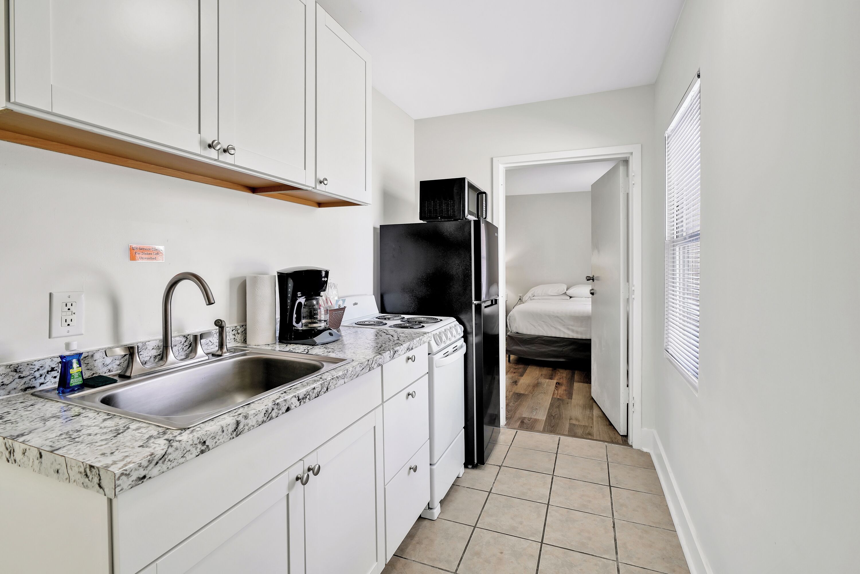 A compact kitchen with white cabinets, a stainless steel sink, a black refrigerator, and a microwave.