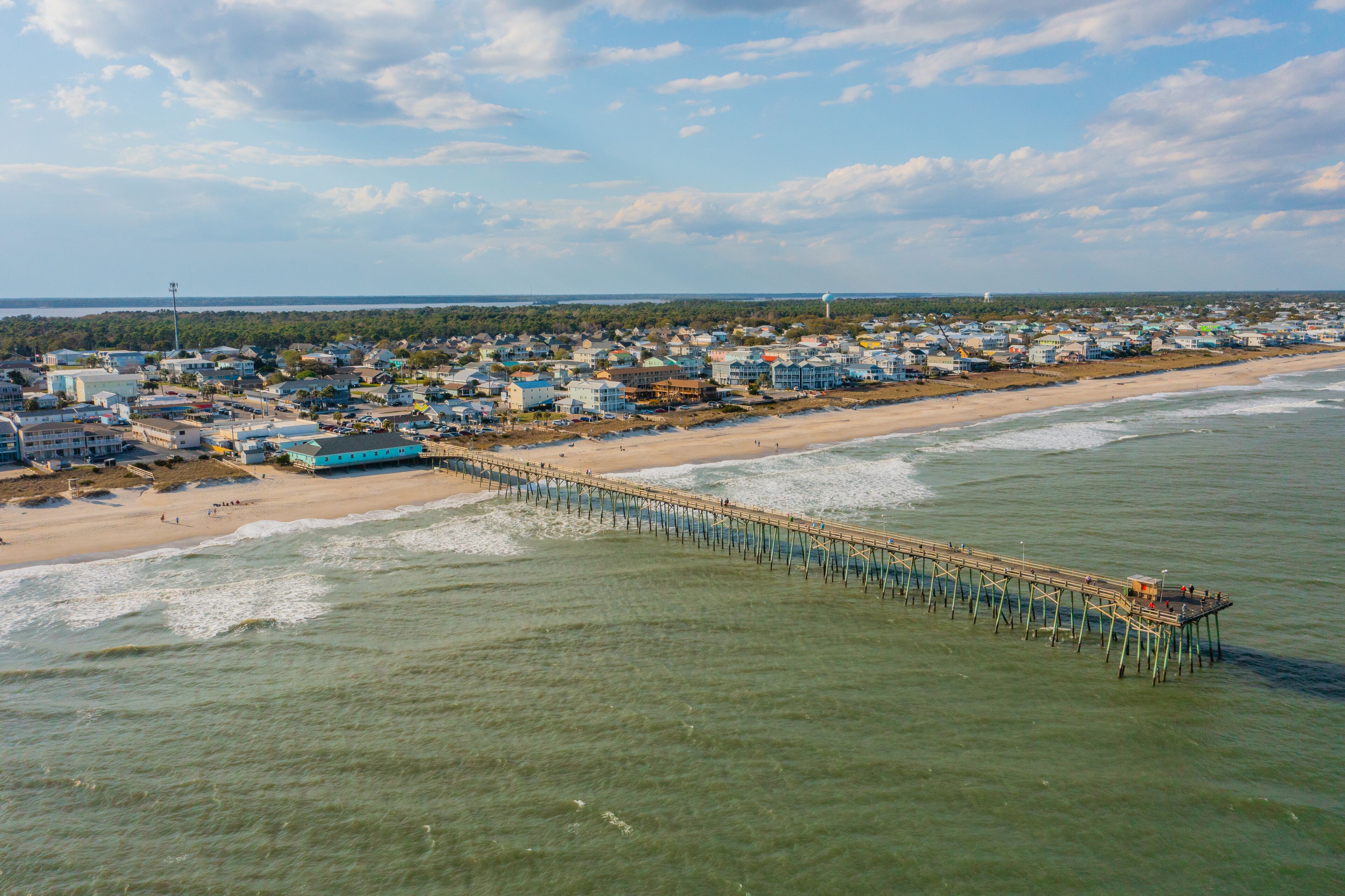 A coastal town with a pier extending into the sea, surrounded by residential buildings and a beach.