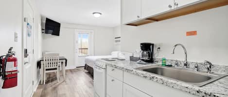 A compact kitchen with white cabinets, a granite countertop, a built-in sink, and a coffee maker.