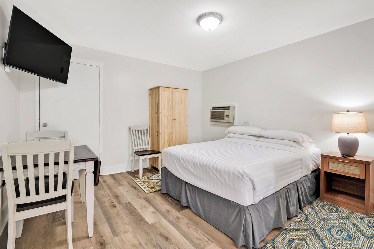 Quarto com cama, escrivaninha, cadeira, guarda-roupa, luminária e ar condicionado.