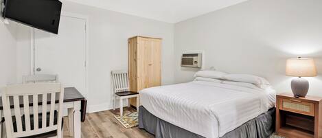A bedroom with a bed, a desk, a chair, a wardrobe, a lamp, and an air conditioning unit.