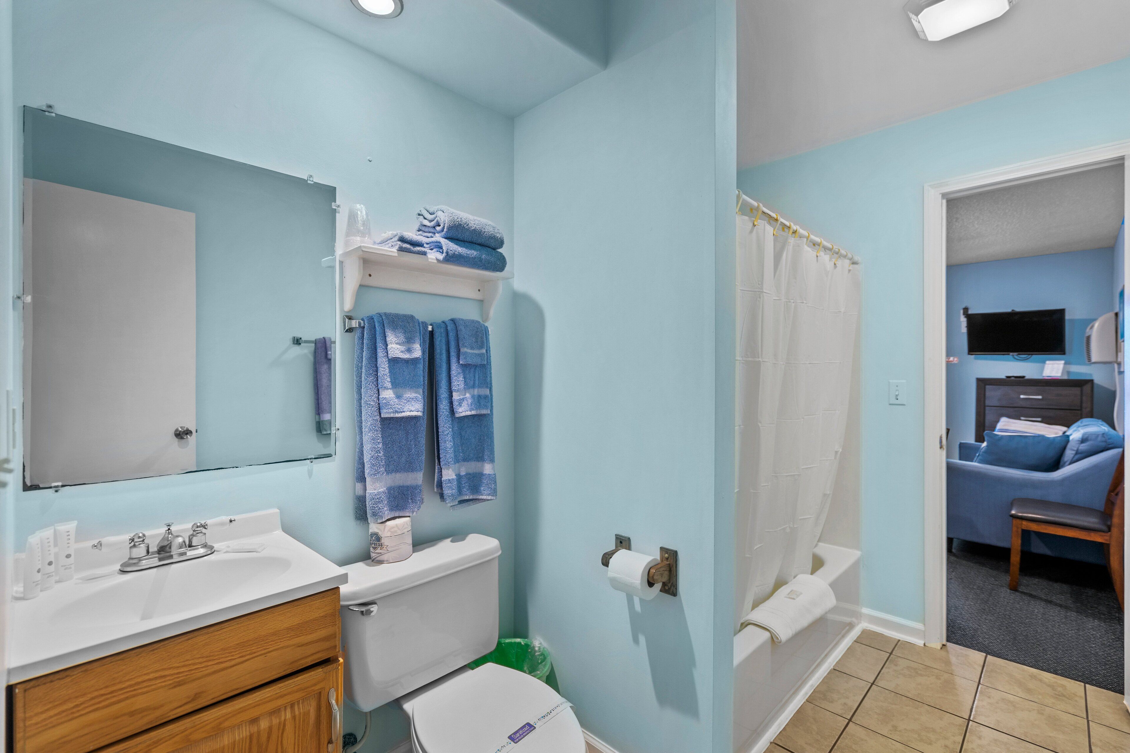 A bathroom with a sink, toilet, and shower curtain. There is a mirror above the sink and a towel rack with towels.