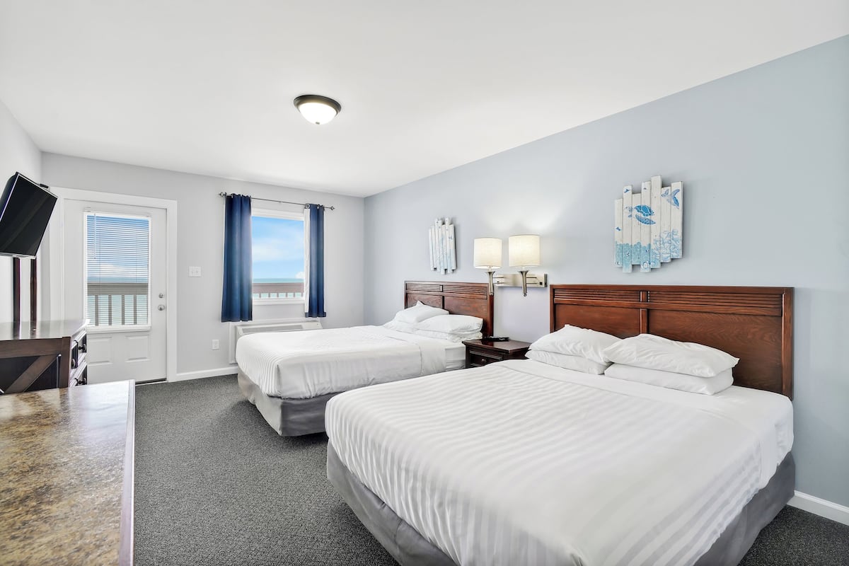 Quarto de hotel com duas camas, uma escrivaninha, uma televisão e uma janela com cortinas.