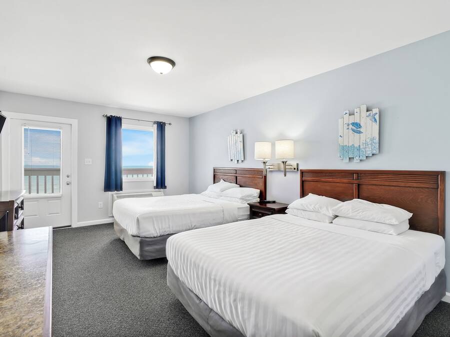 A hotel room with two beds, a desk, a TV, and a window with curtains.