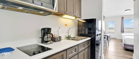 Una cocina moderna con microondas, estufa y refrigerador. Hay un lavamanos con grifo y una cafetera en la encimera. La cocina tiene armarios de madera y una cubierta de color blanco.