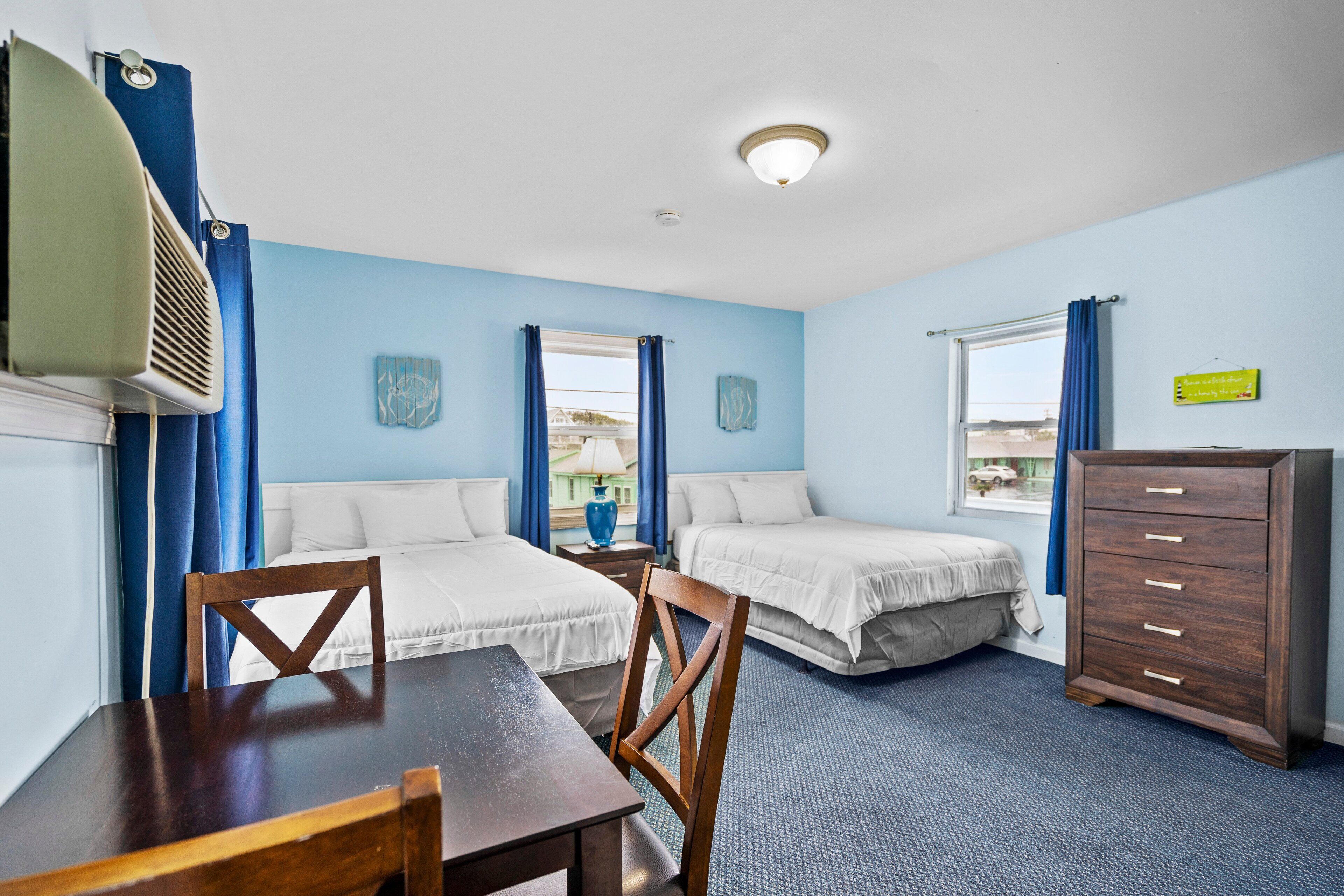 A hotel room with two beds, a wooden dresser, a table, and a ceiling fan.