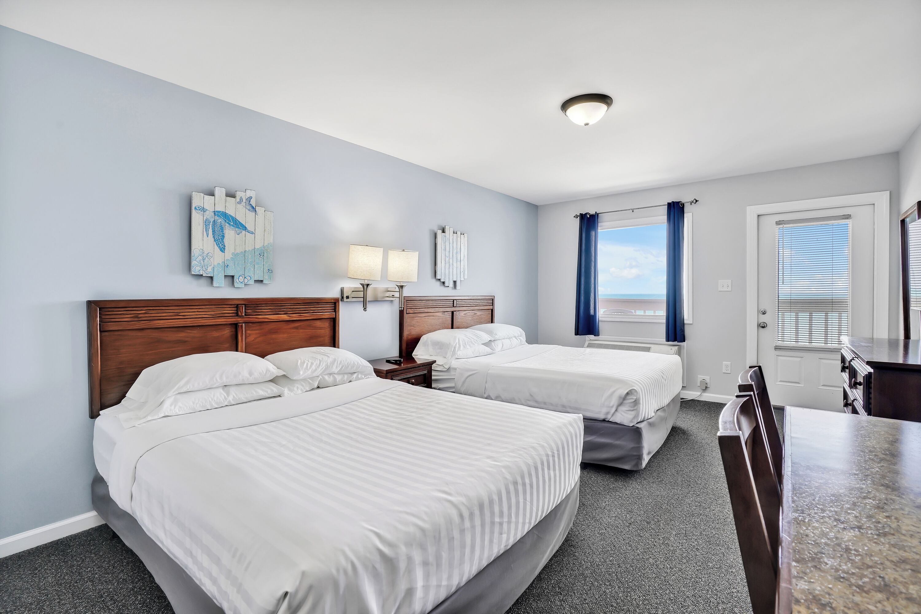 Een hotelkamer met twee bedden, een houten hoofdeinde, een bureau en uitzicht op de lucht door het raam.