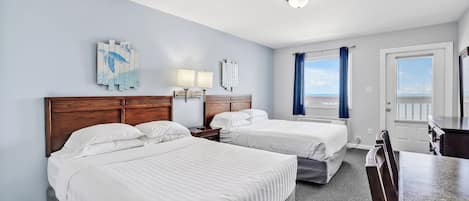 A hotel room with two beds, a wooden headboard, a desk, and a view of the sky through the window.