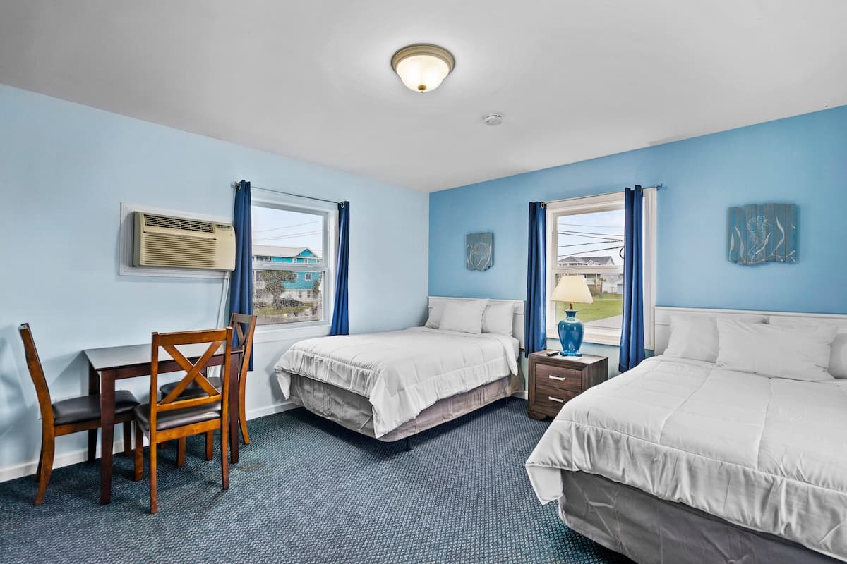 Quarto de hotel com duas camas, uma escrivaninha com cadeira e uma janela com cortinas.