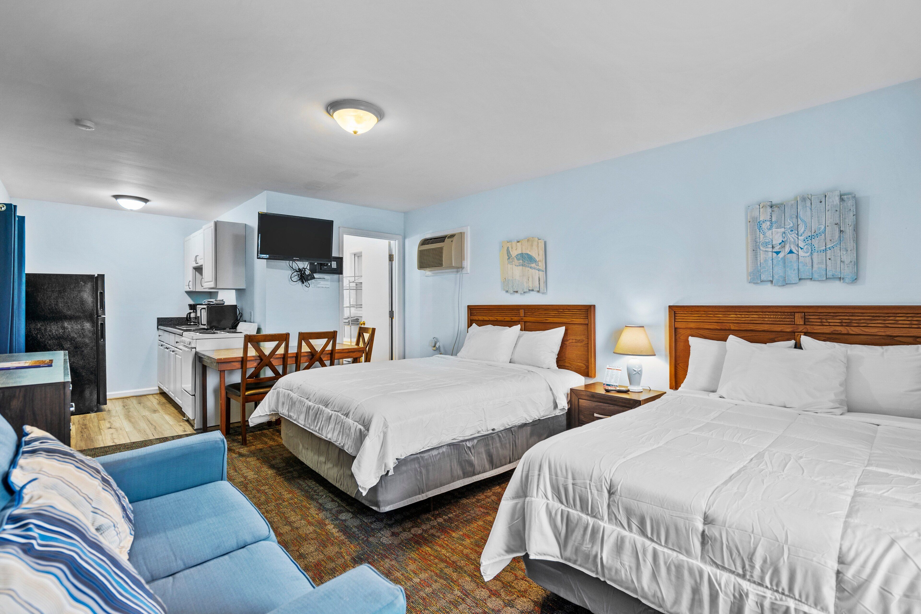 Une chambre d’hôtel avec deux lits, un bureau, une chaise et une kitchenette.