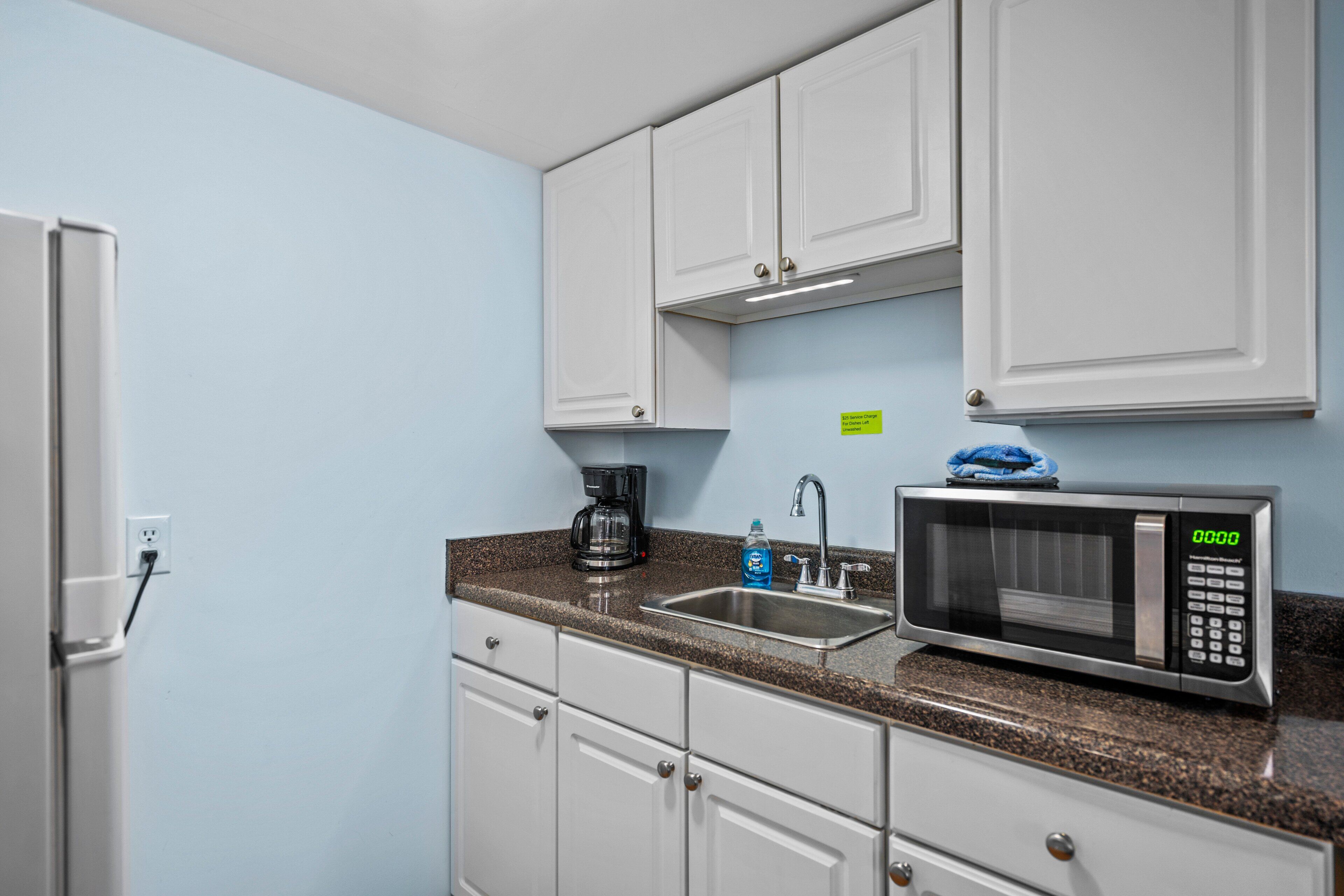 A compact kitchen with white cabinets, a stainless steel sink, a coffee maker, and a microwave.