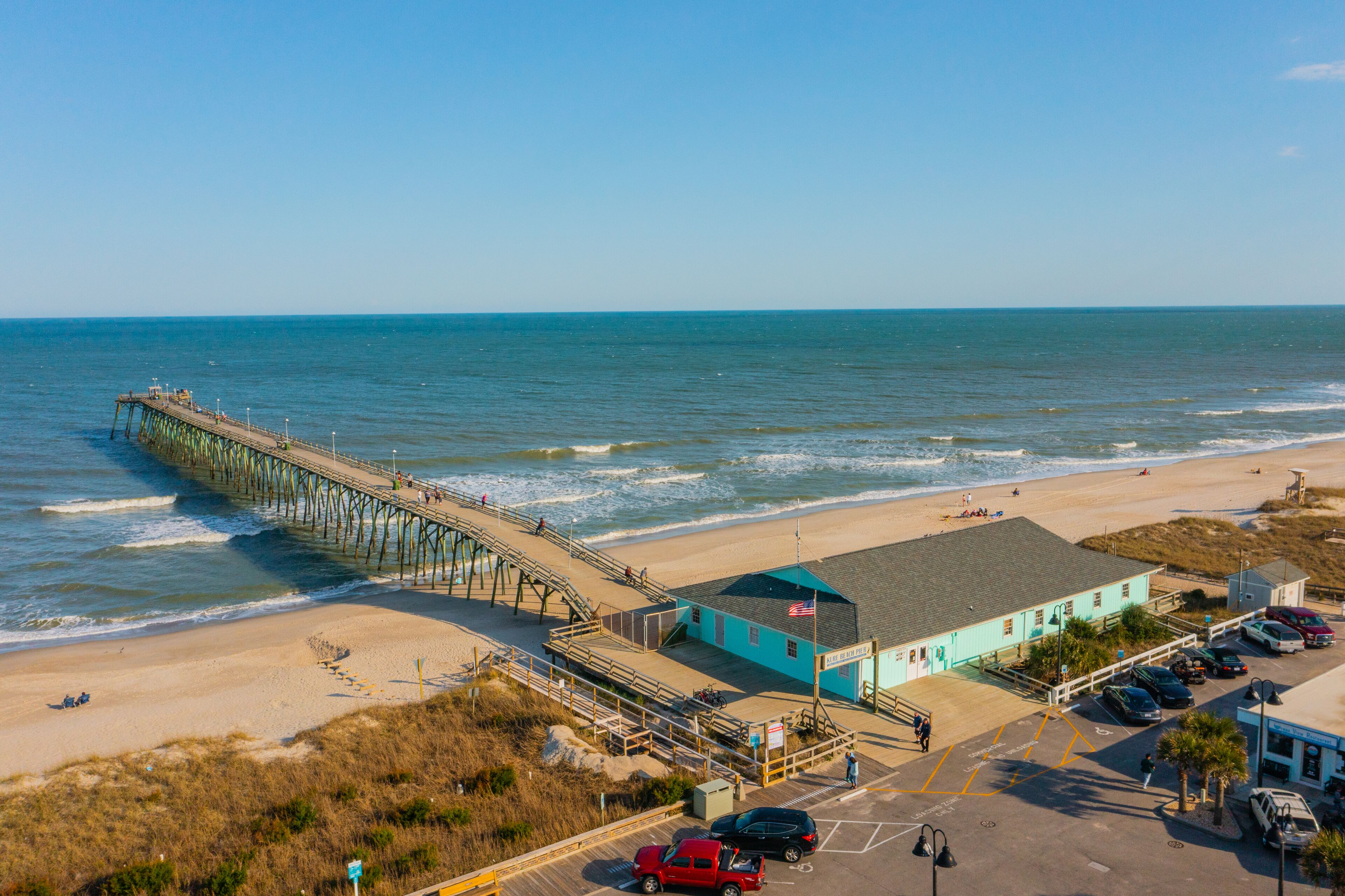 A pier extending into the ocean with a beach and a building adjacent to it.